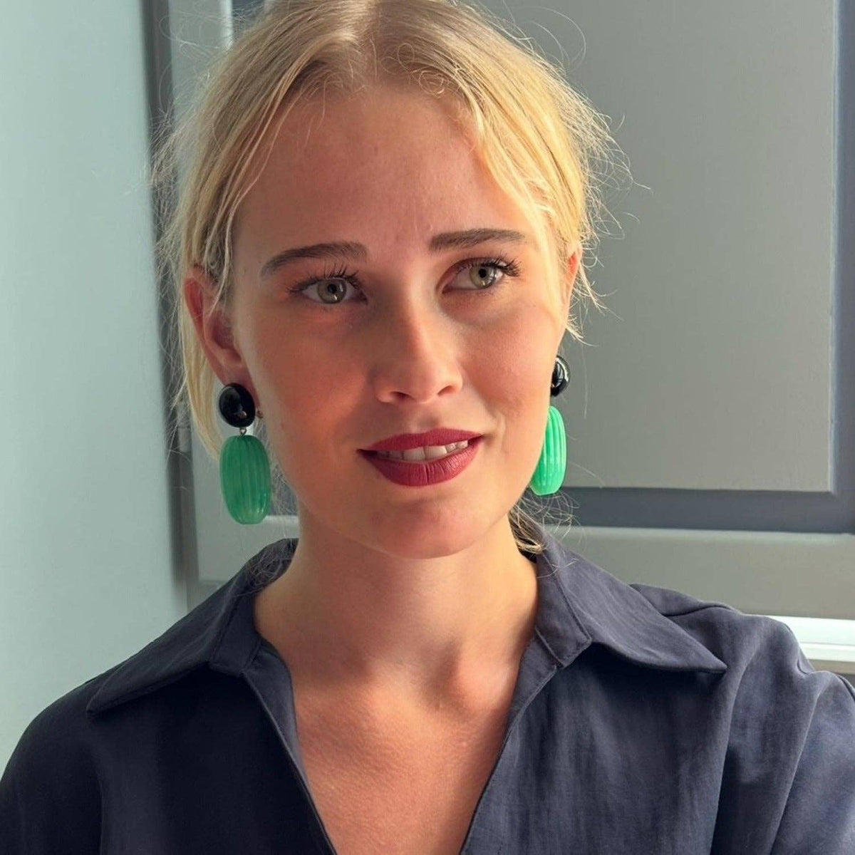 Model wearing clip-on earrings: black round tops with green oval drops