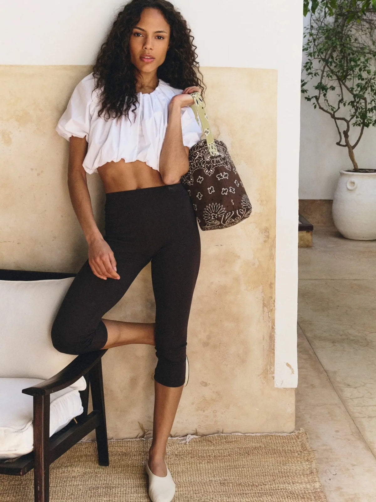 Brown bandana-print bucket bag with beige shoulder strap, worn over the shoulder