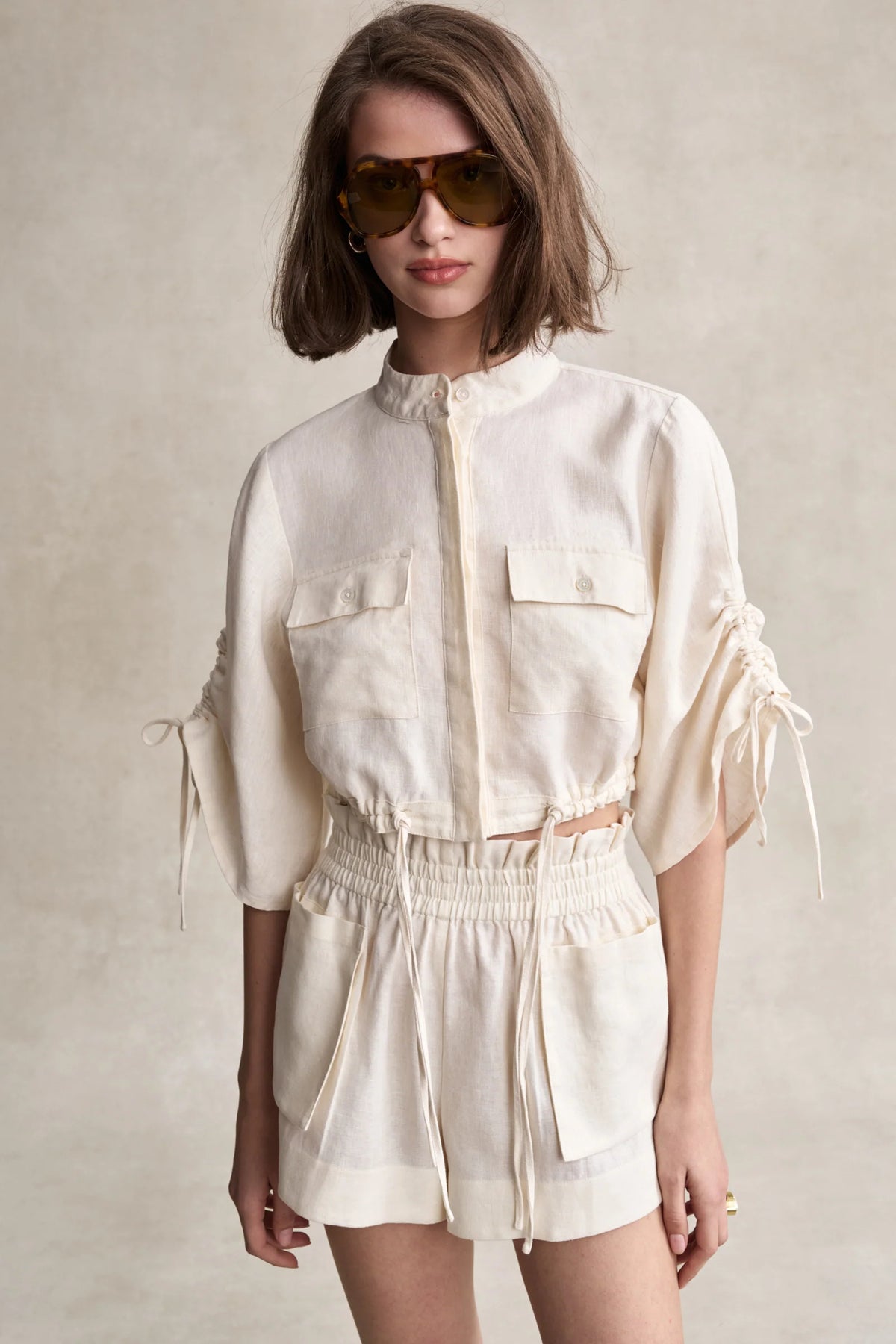 Off-white linen shorts with elastic waistband and front patch pockets, side ties