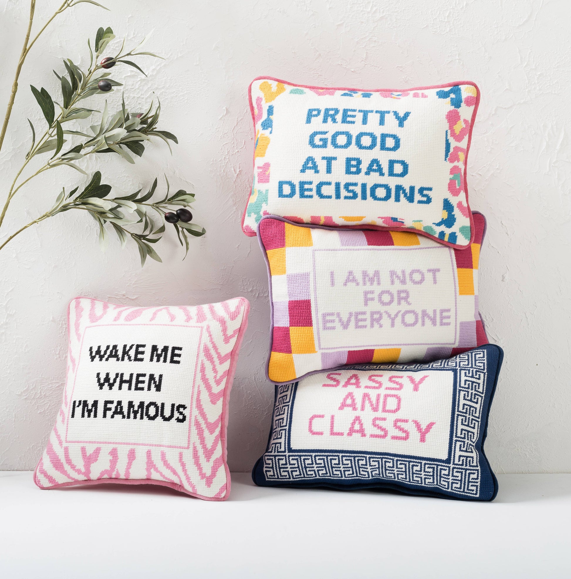 Stacked embroidered throw pillows with blue text, pink border, and colorful accents