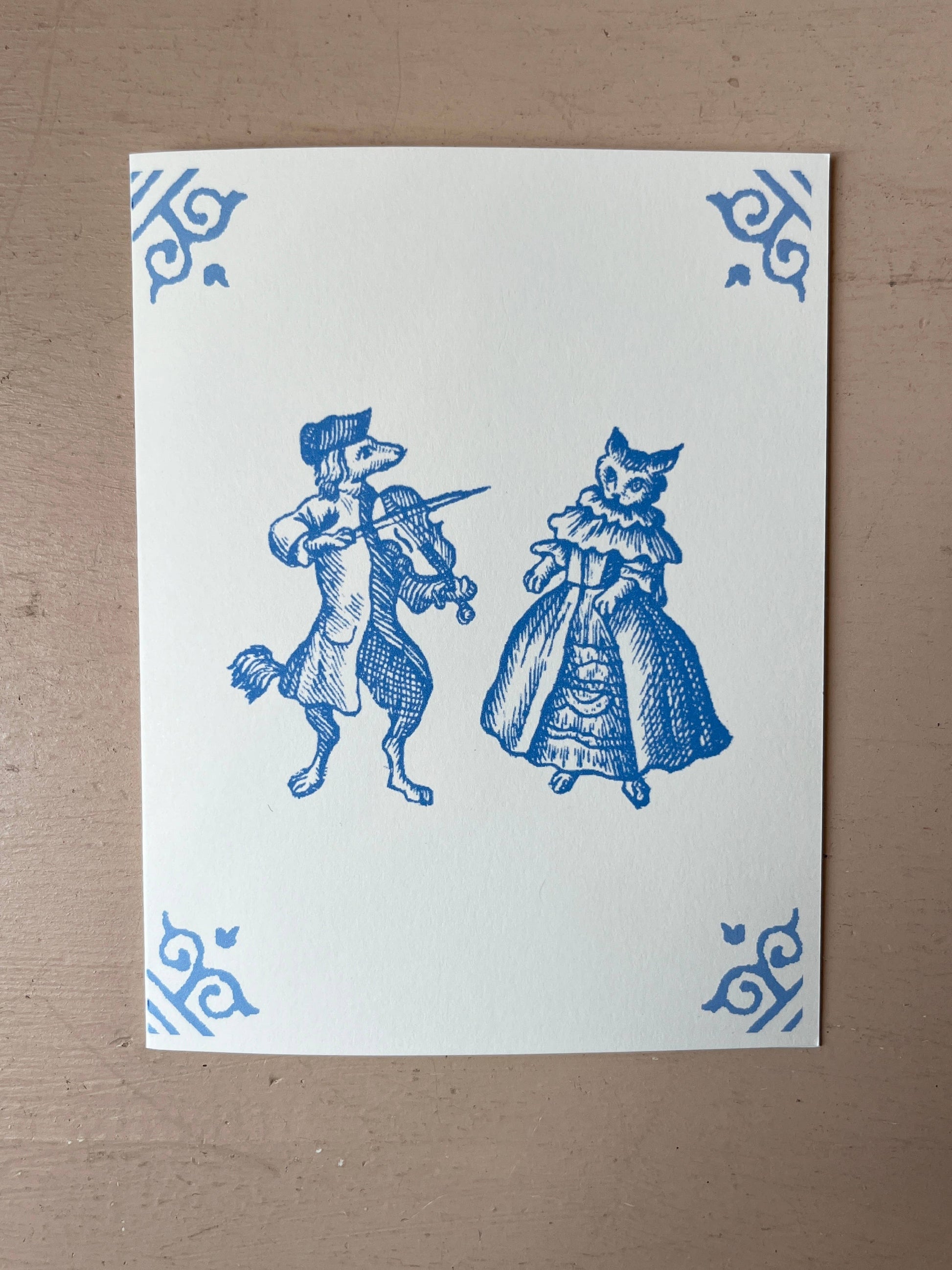 White card with blue illustration of dog musician and cat in dress, ornate corner motifs