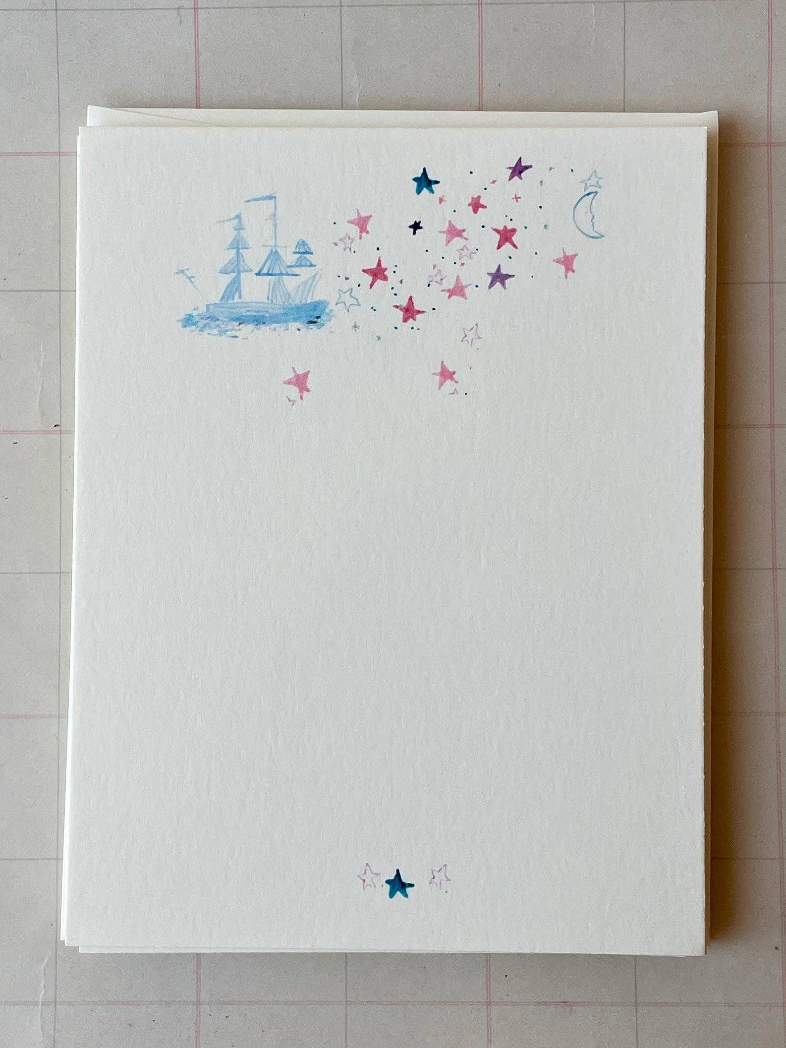 White notecard sheet with blue sailboat and multicolor star constellation with moons