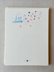 White notecard sheet with blue sailboat and multicolor star constellation with moons