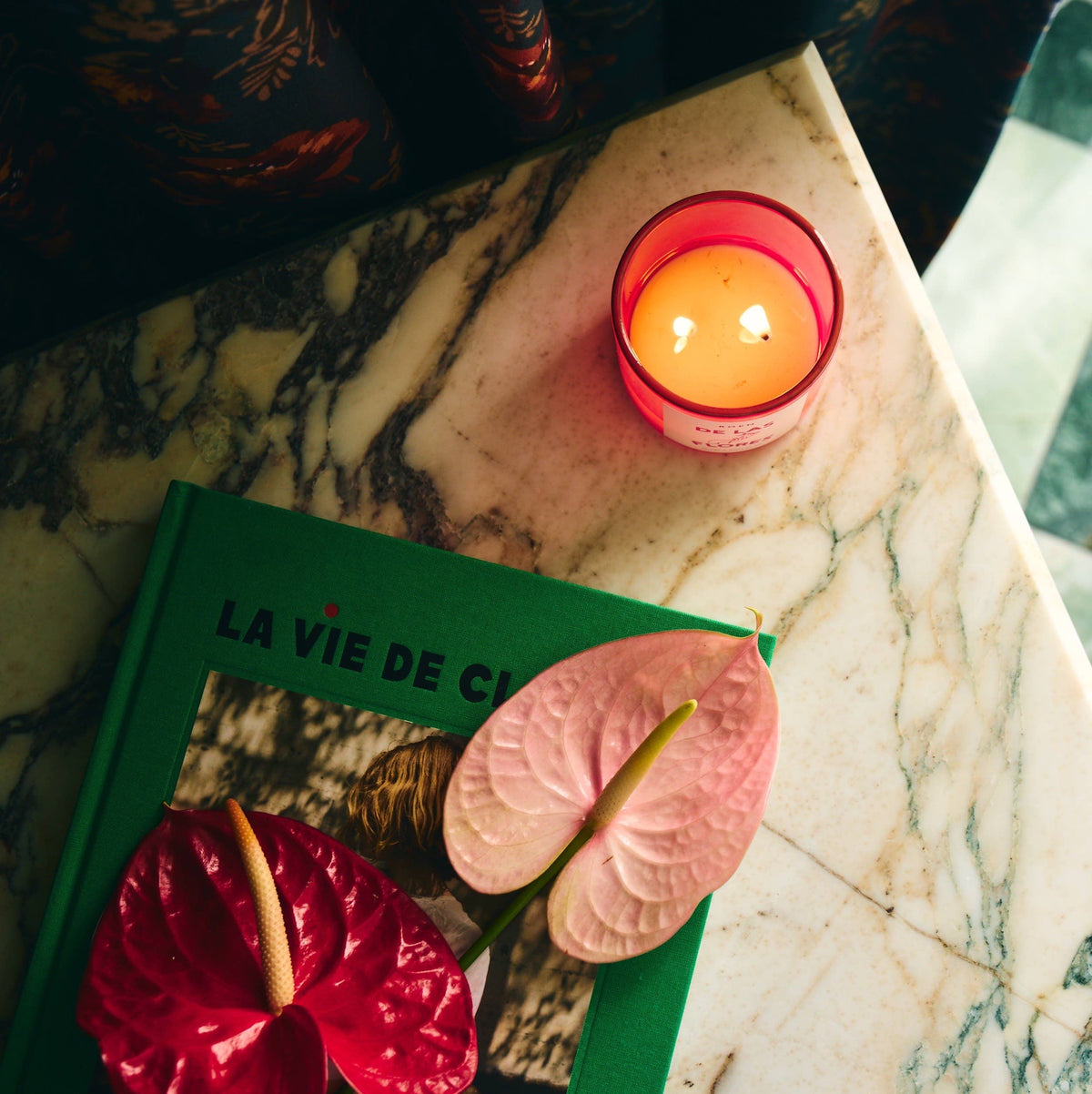 Of the Flowers scented candle in red glass with a lit flame on marble