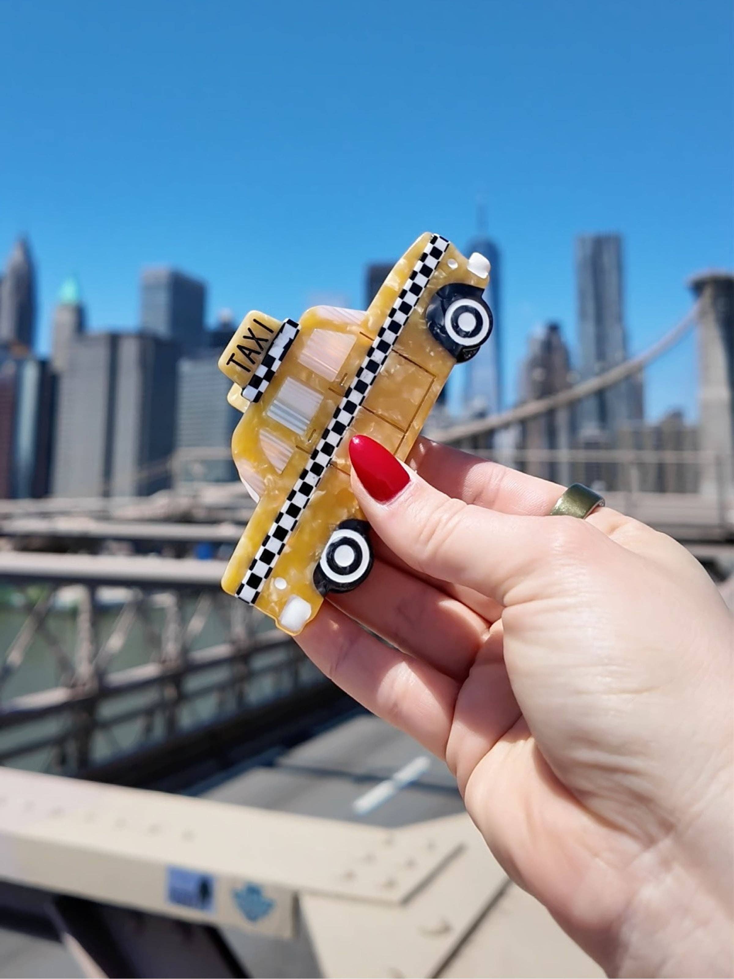 Yellow taxi cab claw hair clip held in hand, with checkered stripe and TAXI sign