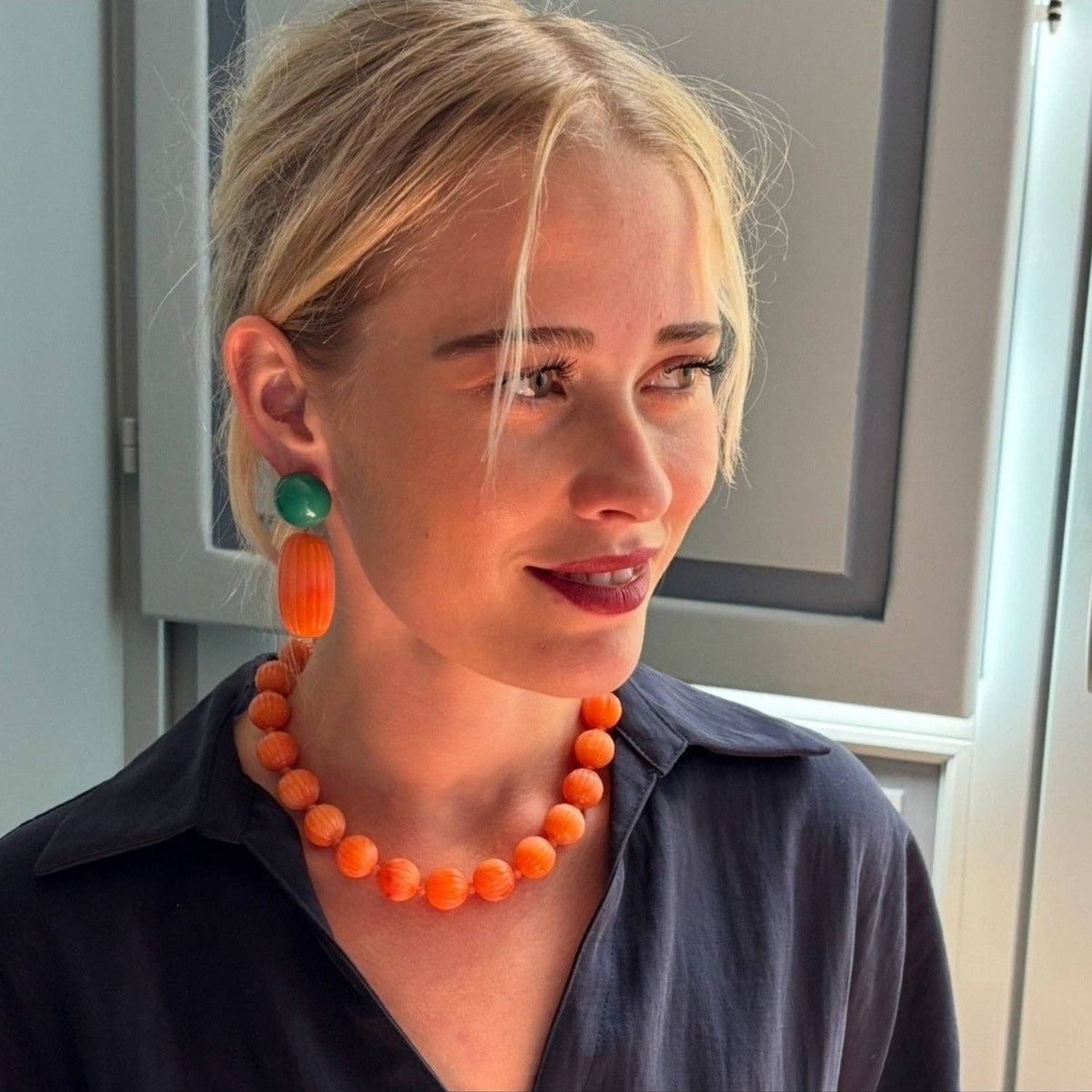 Model wearing pierced earrings: green jade top with orange ribbed coral drop