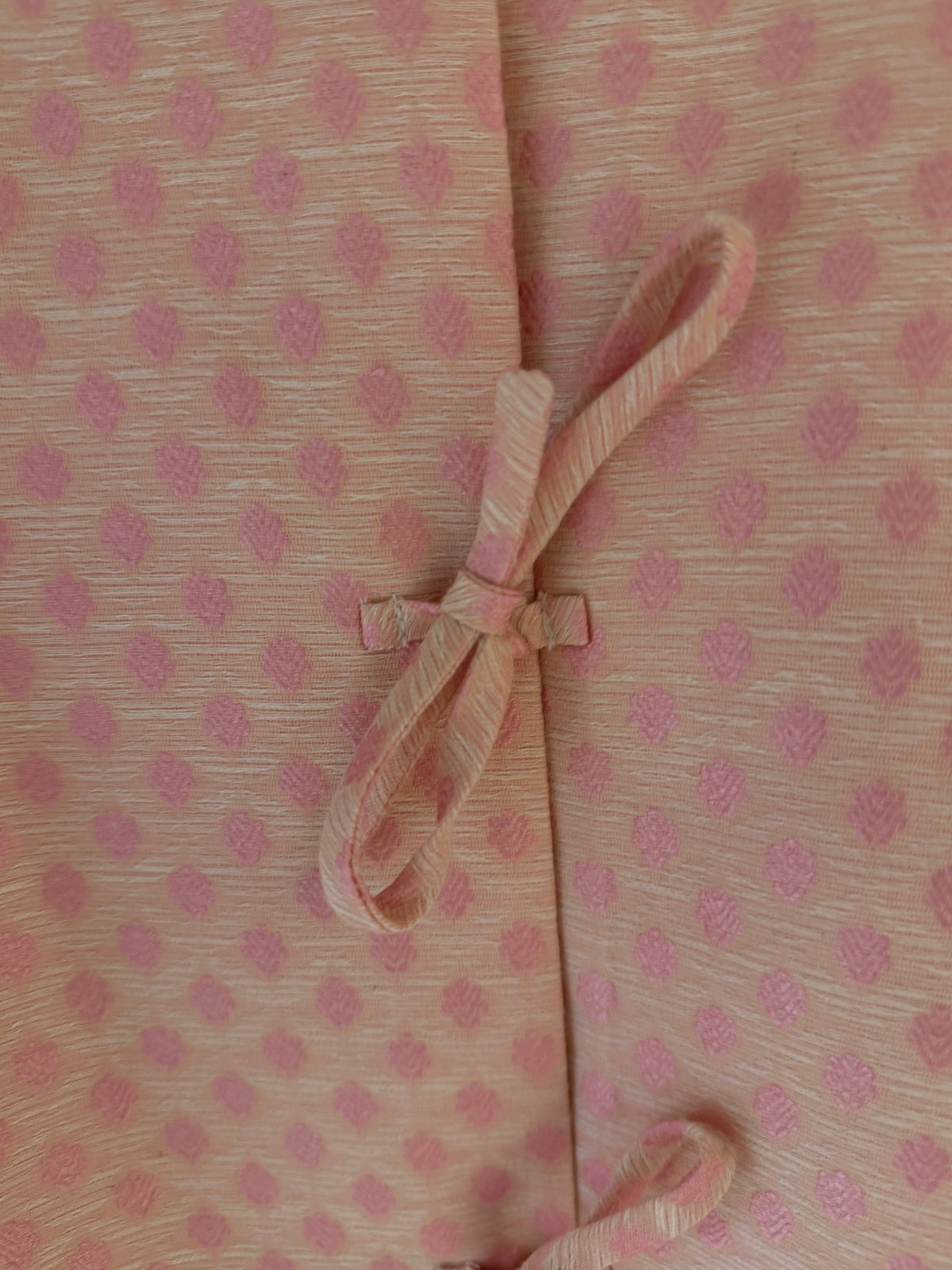 Pink patterned jacket detail with bow-tied front closures and scalloped edges