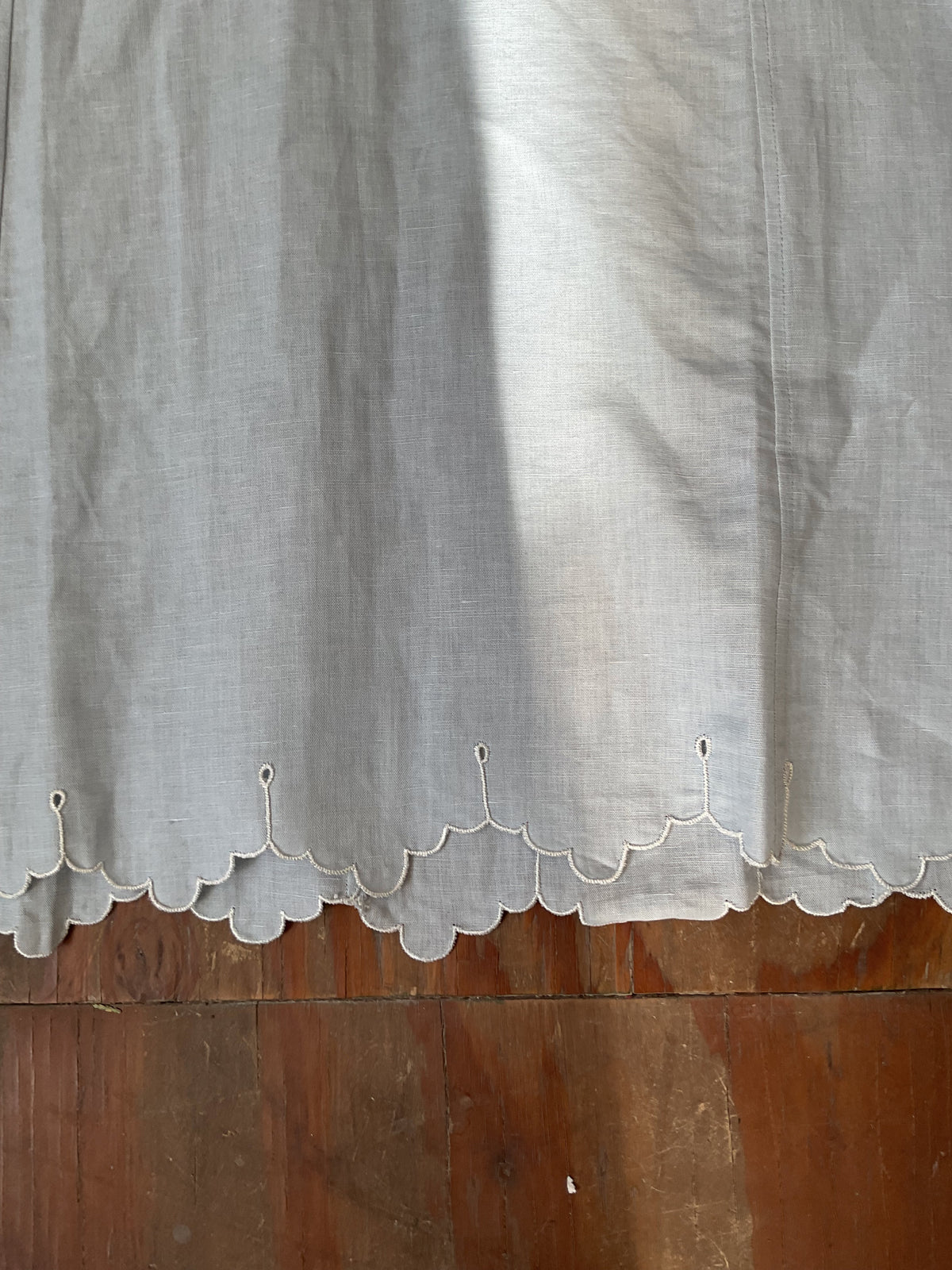 White kaftan hem with scalloped edging and small looped button closures along the bottom