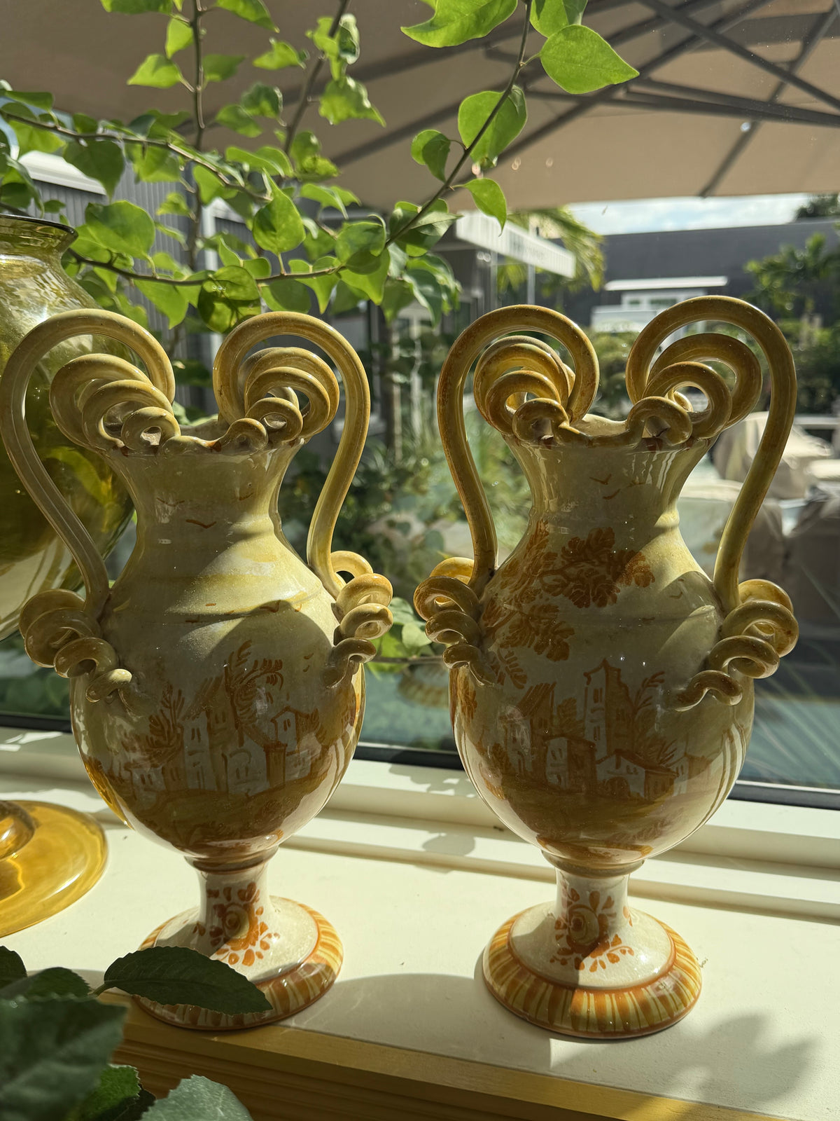 Pair of maiolica ceramic urns with coiled serpent handles, floral and landscape scenes.