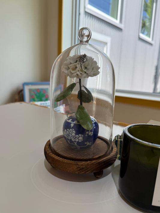 Glass dome with white hydrangea and blue-and-white ceramic pot on wooden base