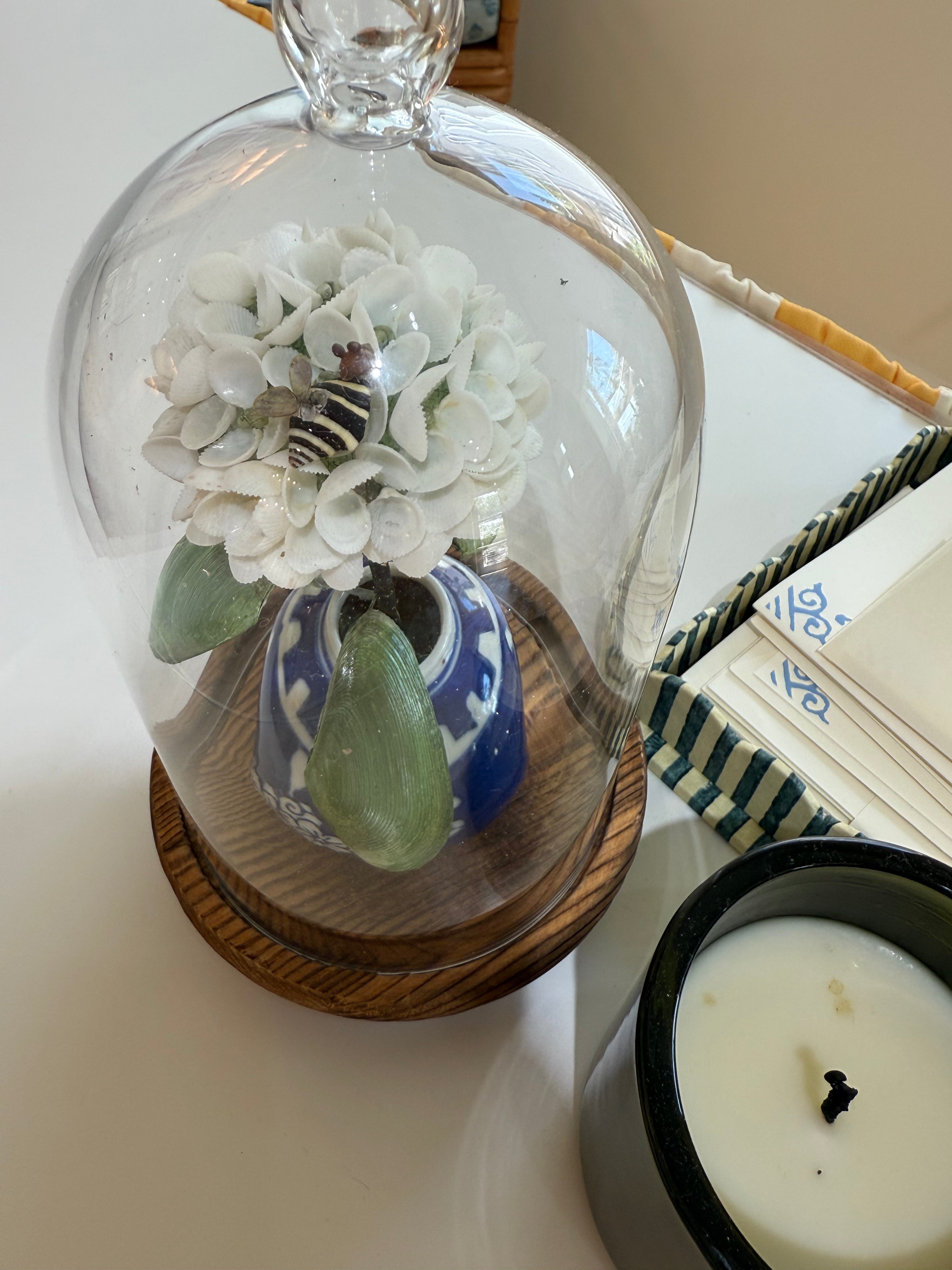 Glass dome with white hydrangea and blue-and-white pot on round wood base