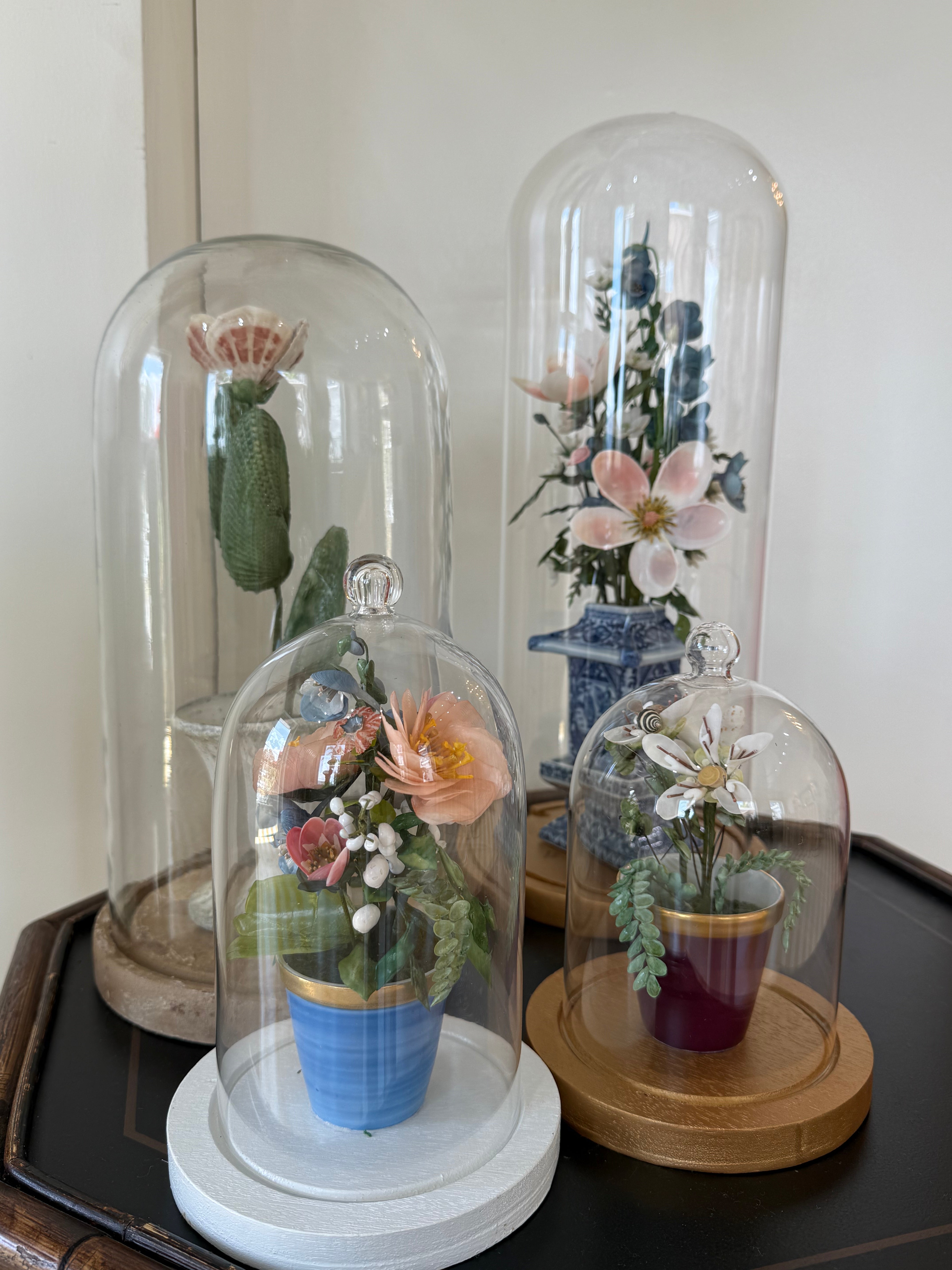 Floral centerpiece in clear glass dome with blue-and-white pedestal pot, with other domes.