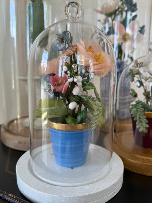 Mini floral arrangement under a glass dome with a blue ceramic base and mixed blooms