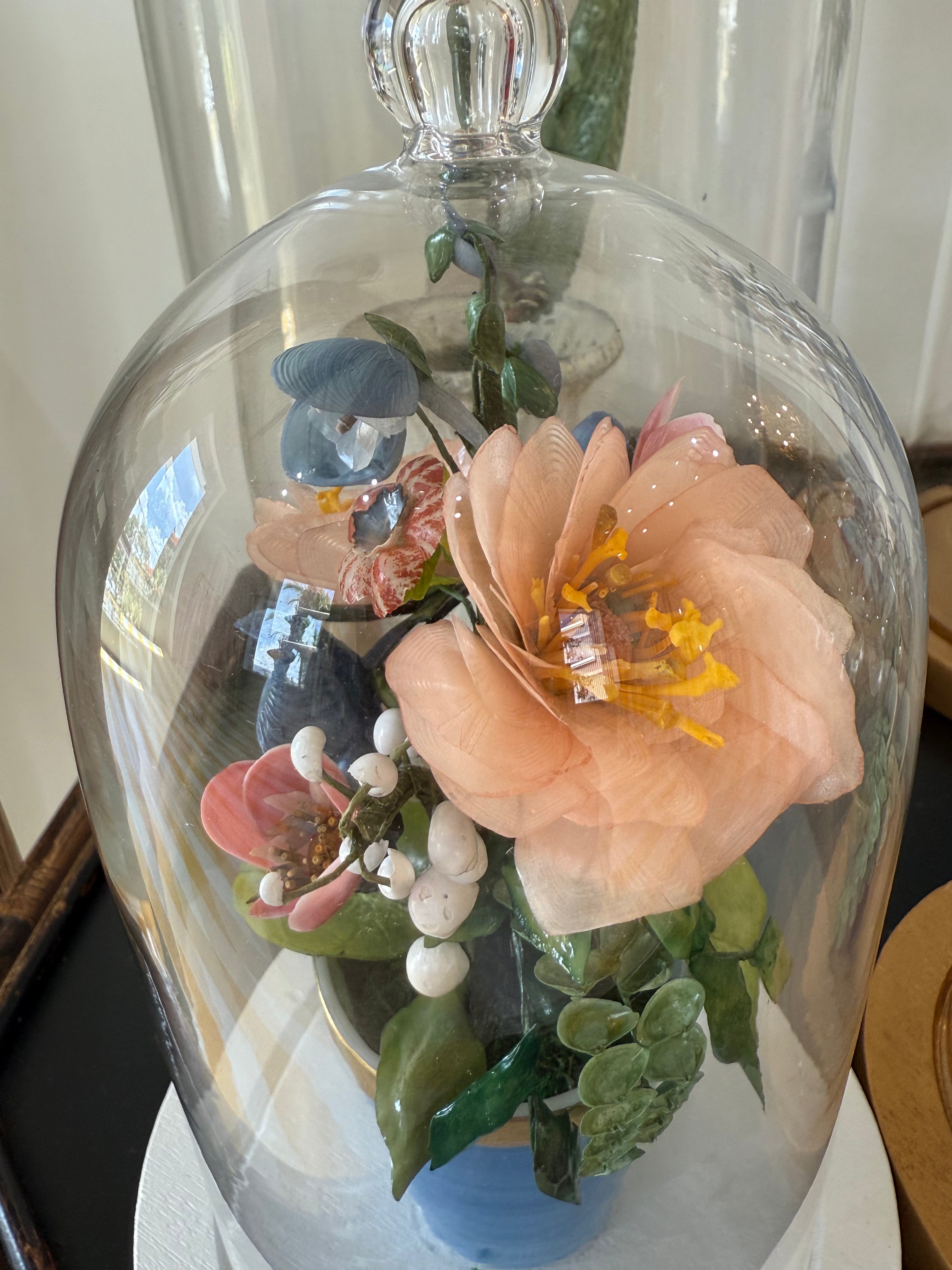 Mini blue pot floral arrangement under glass dome, close-up of peach bloom and greenery