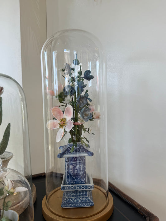 Floral arrangement in blue-and-white vase under glass dome with pink and blue flowers