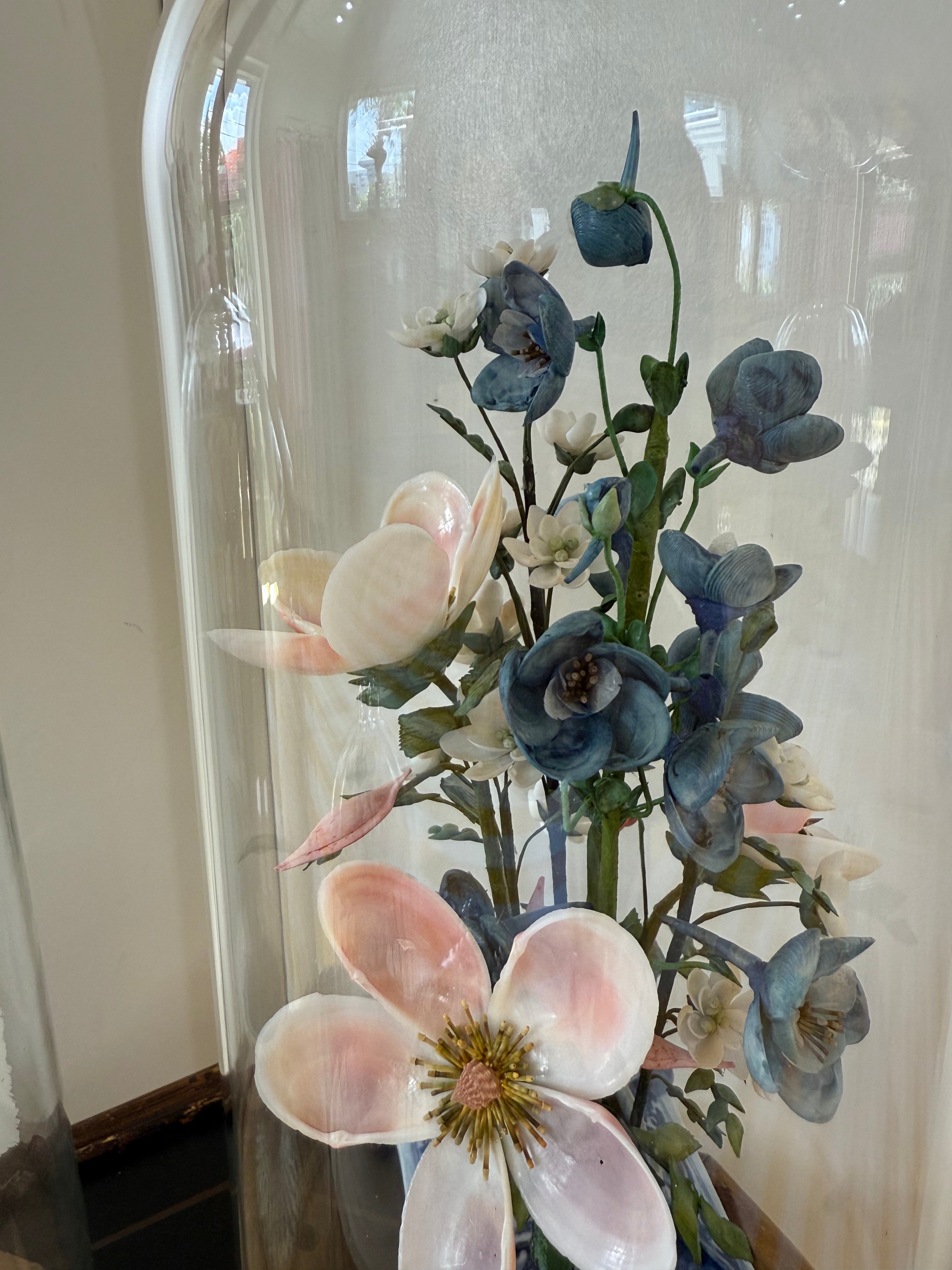 Blue and white floral arrangement under glass dome with pastel pink and blue blooms.