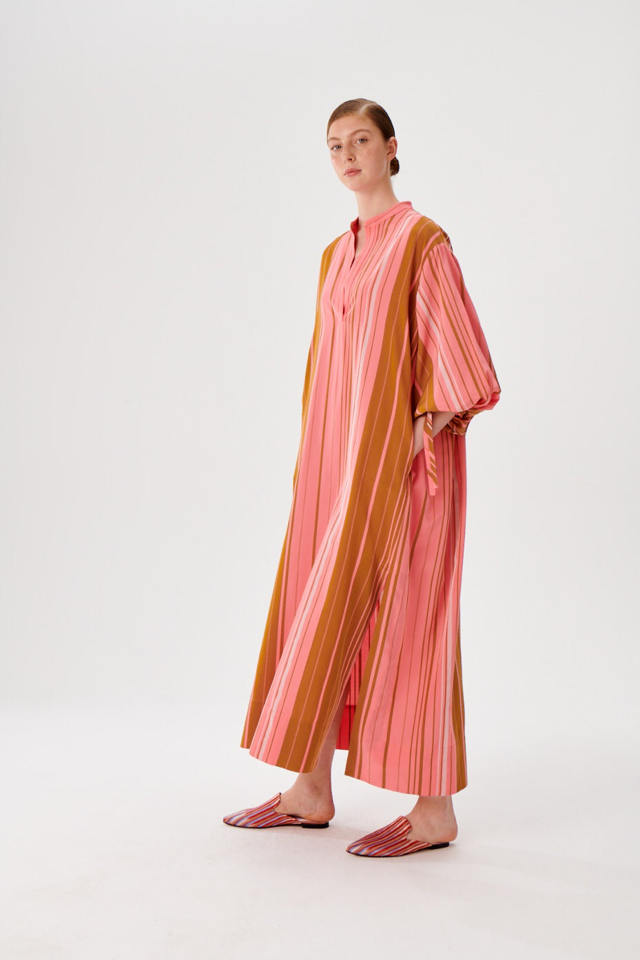 Maxi caftan dress side view, pink and rust vertical stripes, split neckline, flowing wide sleeves.