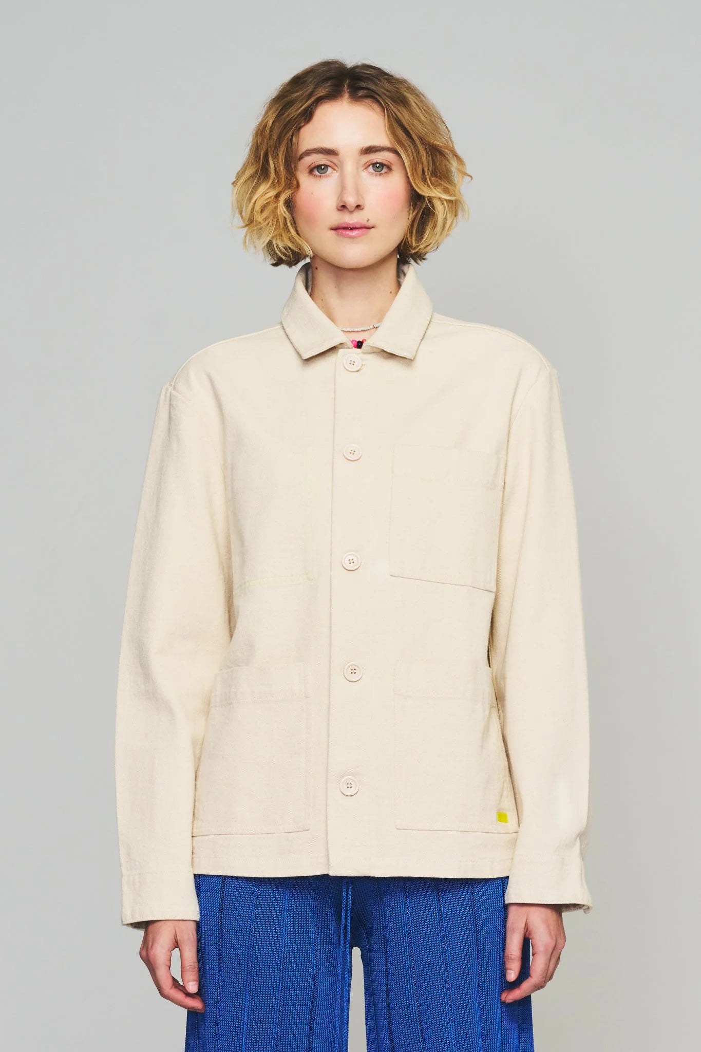 Cream chore coat with pointed collar, button front, chest pocket, small yellow patch