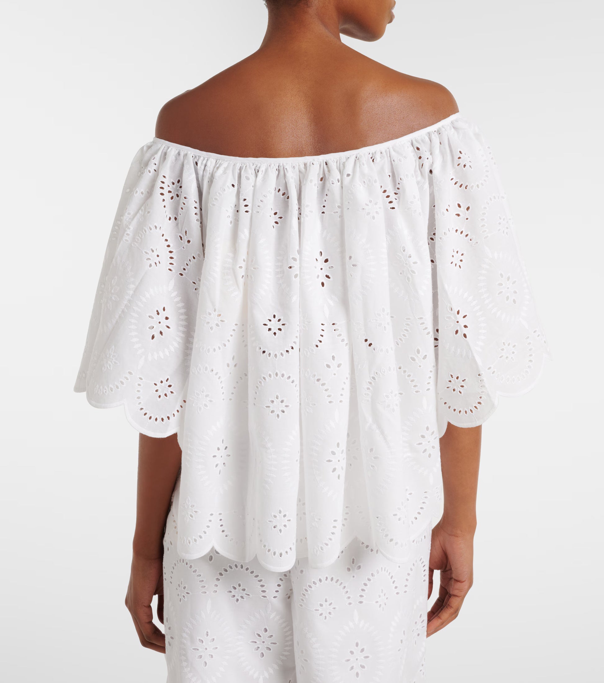 White eyelet off-shoulder top with gathered neckline and scalloped back hem