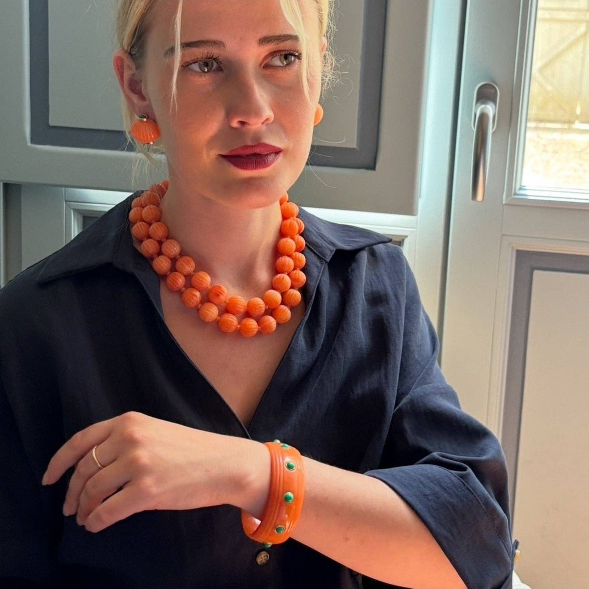Woman wearing coral orange carved resin bead necklace with round melon-style beads