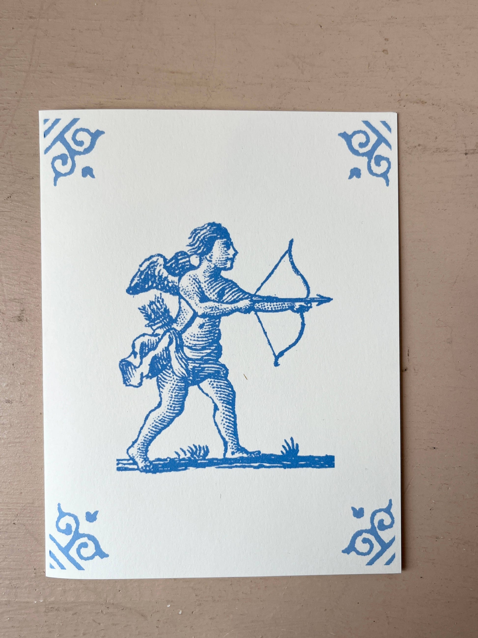 White card with blue illustration of an archer dog holding a bow and arrow, corner motifs