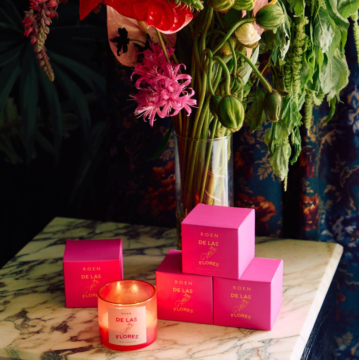 Of the Flowers candle jar with ROEN branding and pink gift boxes on marble