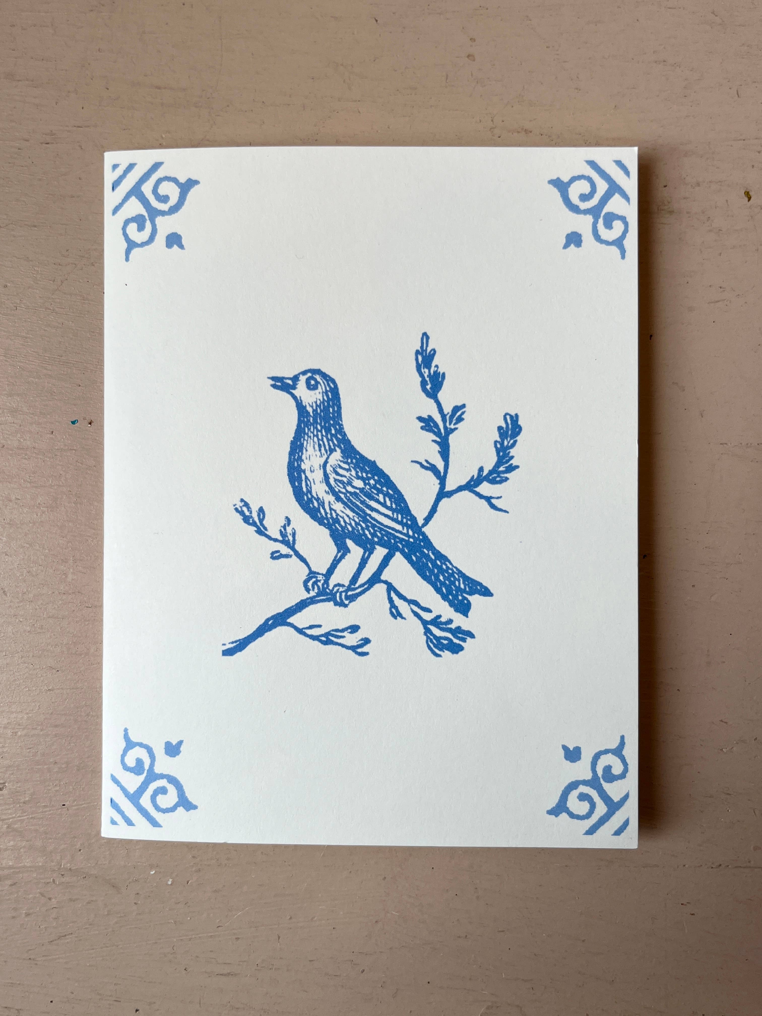 White card with blue bird illustration perched on a branch, ornate corner motifs