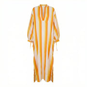 Yellow maxi caftan dress with vertical orange stripes, V-neck, long sleeves, tied cuffs.