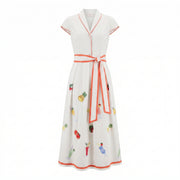 White garden dress with V-neck, button front, orange trim, fruit print and tied waist.